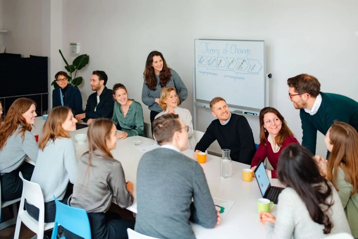 A diverse group of individuals engaged in discussion around a table in a meeting room, promoting Team Value for Good.