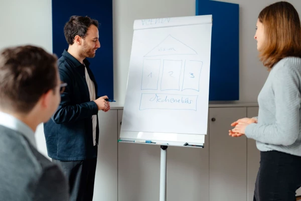 A man and woman stand together in front of a whiteboard, engaged in discussion or presentation.